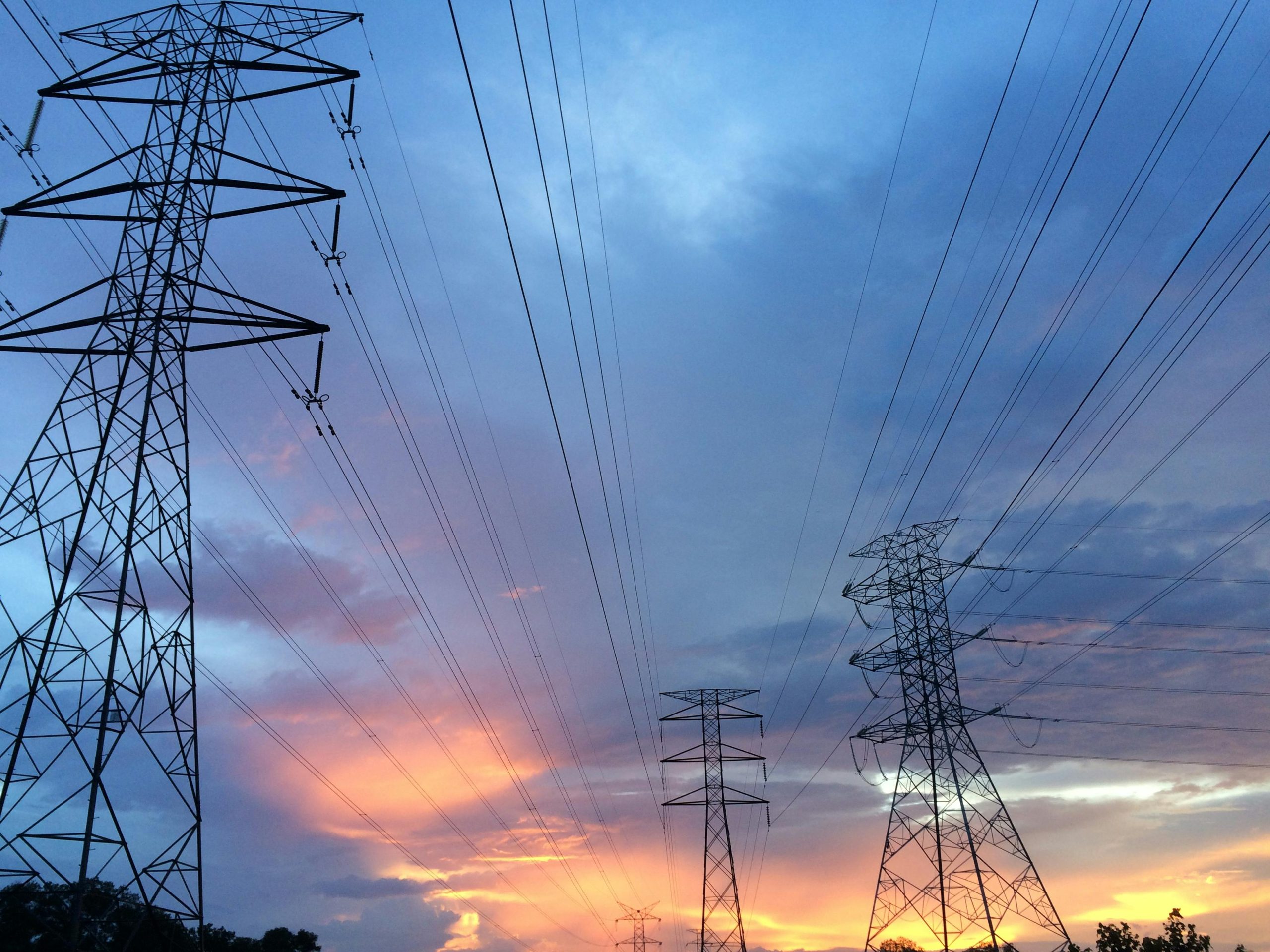 A scenic view of high voltage power lines silhouetted against a vibrant sunset sky.