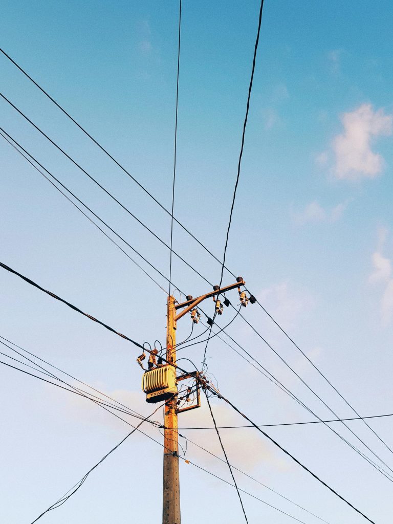 Low-angle shot of electricity poles and wires against a clear blue sky.