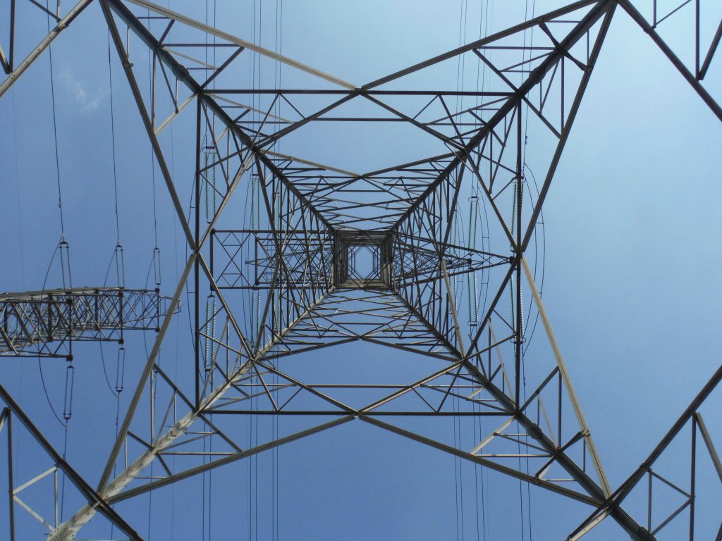 A striking low angle perspective of an electricity tower with a clear blue sky background.