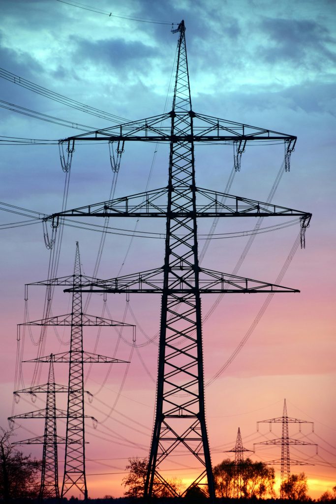 Electricity pylons silhouetted against a dramatic sunset sky, showcasing high voltage transmission.